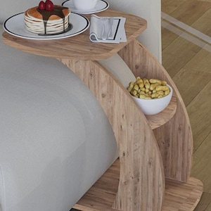 Puede incluir: Una mesa auxiliar de madera en forma de C con dos niveles. El nivel superior contiene un plato de panqueques con sirope y fresas, una taza de café y una servilleta con cubiertos. El nivel inferior tiene un cuenco de cacahuetes.