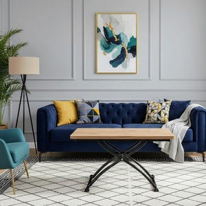 Puede incluir: Un salón con un sofá azul marino capitoné, cojines amarillos y estampados, y una mesa de centro de madera con patas de metal negro. Un cuadro abstracto enmarcado cuelga de la pared gris. La alfombra tiene un patrón geométrico.