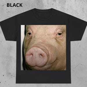 Puede incluir: Camiseta negra con una imagen en primer plano de la cara de un cerdo. Se ven el hocico y los ojos del cerdo, con la palabra "BLACK" impresa en la parte superior de la camiseta.