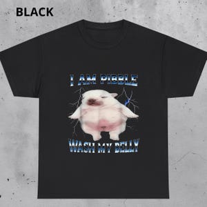 Pode incluir: Camiseta preta com uma imagem de desenho animado de uma criatura branca e rechonchuda e o texto "I AM PIBBLE WASH MY BELLY" em azul e branco. O design inclui gráficos de raios.