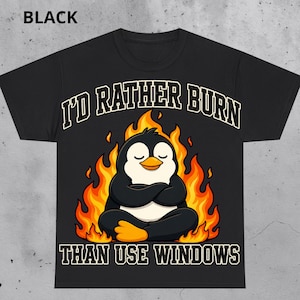 May include: A black short-sleeve t-shirt featuring a graphic of a penguin sitting in a meditative pose surrounded by orange and yellow flames. The text "I'D RATHER BURN" appears above the penguin and "THAN USE WINDOWS" appears below it.