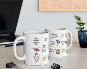 Może przedstawiać: Dwa białe ceramiczne kubki z czarnym tekstem i kwiatowymi wzorami. Jeden kubek zawiera tekst "Bóg jest w niej, ona nie upadnie" i "Bóg jest większy niż wzloty i upadki". Drugi kubek ma tekst "Łaska przyniosła mnie tutaj i przez łaskę zostanę".