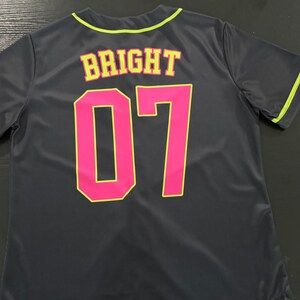 May include: A dark gray short-sleeved jersey with neon yellow trim on the collar and sleeves. The back features the word BRIGHT in yellow letters with pink outlines, positioned above the large number 07 in solid pink with yellow outlines.