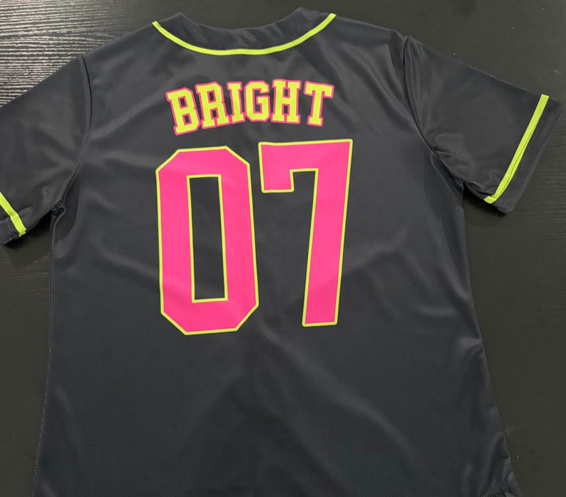 May include: A dark gray short-sleeved jersey with neon yellow trim on the collar and sleeves. The back features the word BRIGHT in yellow letters with pink outlines, positioned above the large number 07 in solid pink with yellow outlines.