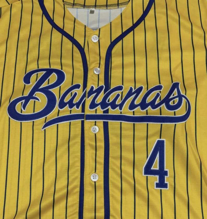 May include: A yellow baseball jersey with thin vertical black pinstripes, featuring the word Bananas in a blue script font across the chest and the number 4 in blue block digits below. The shirt has a button-down front with white buttons.