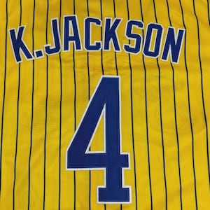 May include: A yellow sports jersey featuring thin vertical black pinstripes. The back displays the name K. JACKSON in bold blue letters with white outlines, positioned above the large blue number 4, which also features a white outline.