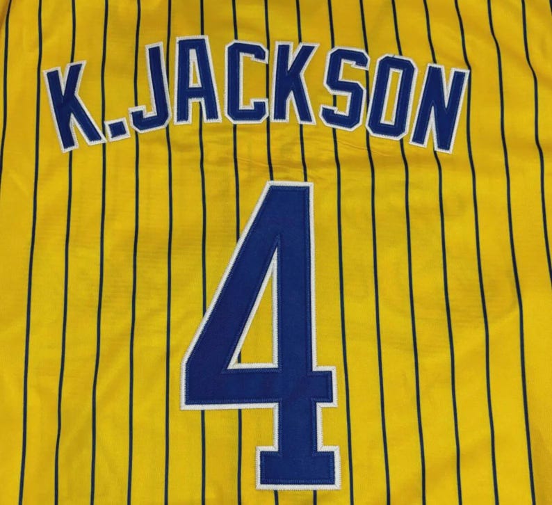 May include: A yellow sports jersey featuring thin vertical black pinstripes. The back displays the name K. JACKSON in bold blue letters with white outlines, positioned above the large blue number 4, which also features a white outline.