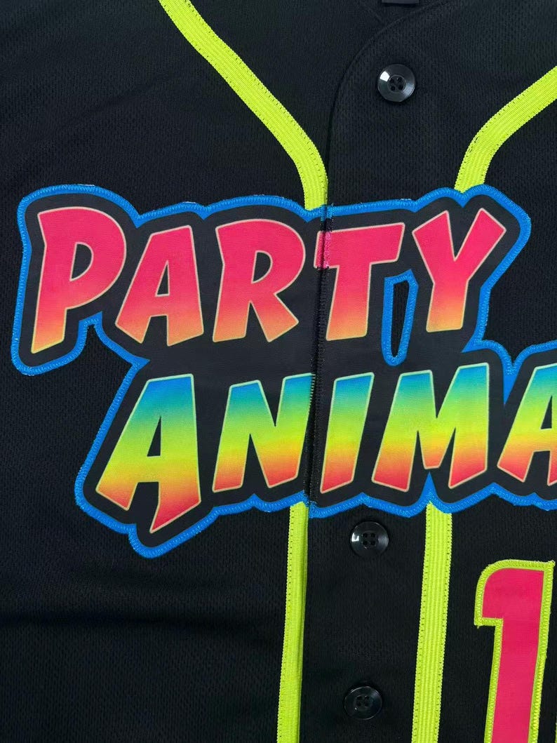 May include: A black button-down baseball jersey featuring neon yellow piping along the placket and collar. The front displays the text PARTY ANIMAL in a gradient of pink, orange, and yellow with a bright blue outline, plus a partial pink number 1.