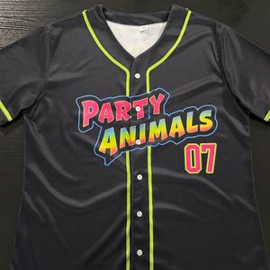 May include: A black short-sleeve button-down baseball jersey featuring neon green piping along the collar, placket, and sleeves. The front displays the text "PARTY ANIMALS" in a colorful gradient font with a blue outline and the number "07" in pink.