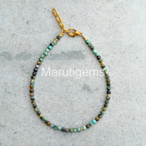Può includere: Un delicato braccialetto di perline con piccole pietre sfaccettate color turchese con motivi a matrice scura, intervallate da minuscoli distanziatori metallici dorati. Il braccialetto include una chiusura a moschettone dorata e una catenella di estensione.
