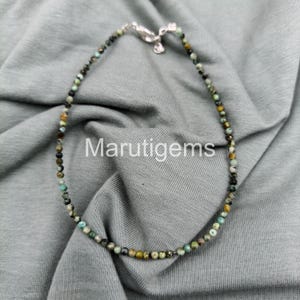 Könnte beinhalten: Eine zarte Perlenkette mit kleinen, runden Perlen in Grün-, Braun- und Gelbtönen. Die Kette ist an einem dünnen Band aufgereiht und hat einen silberfarbenen Verschluss. Der Text "Marutigems" ist auf dem grauen Hintergrund zu sehen.