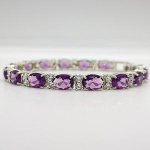 May include: A silver-toned link bracelet featuring a repeating pattern of oval-cut purple amethyst gemstones alternating with small, clear, round-cut white stones set in a metallic frame, arranged in a continuous circular design.