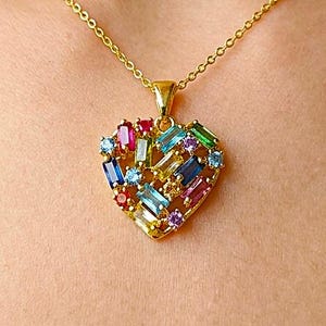 May include: A gold chain necklace featuring a heart-shaped pendant. The pendant is encrusted with a variety of multi-coloured baguette and round-cut gemstones, including shades of blue, red, green, yellow, and purple set in a gold-tone frame.