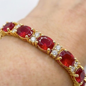 May include: A gold bracelet featuring a series of oval-cut red gemstones alternating with pairs of small, round, clear white stones. The metal setting is yellow gold, and the design consists of a repeating pattern of red and white stones.