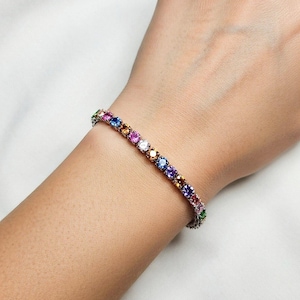 Pu&ograve; includere: Un braccialetto tennis con una fila di pietre preziose colorate. Il braccialetto presenta una variet&agrave; di colori, tra cui rosa, viola, blu, giallo e verde. Le pietre sono incastonate in una fascia d'argento o platino.