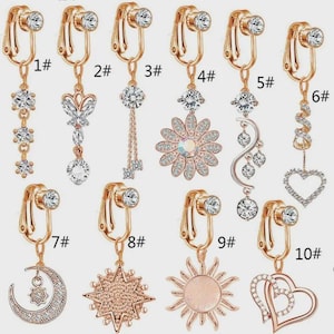 Puede incluir: Colección de diez pendientes de clip con diferentes diseños. Los pendientes presentan metal dorado y cristales transparentes. Los diseños incluyen formas florales, celestiales y geométricas, cada uno numerado.