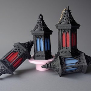 May include: Three black decorative lanterns with intricate gothic-style detailing. One lantern is upright, another is leaning, and the third is lying on its side. The windows of the lanterns are red and blue.