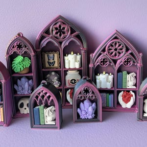 May include: A collection of miniature gothic-style shelves in shades of purple and black, each filled with decorative items. The shelves hold books, crystals, candles, and other small figurines, creating a whimsical display.