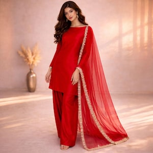 May include: A vibrant red ensemble featuring a long-sleeved tunic and wide-leg pants. A sheer red scarf with gold trim drapes over the shoulder. The outfit is a solid color, creating a sleek and elegant look.