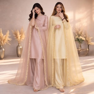 May include: Two women wearing matching formal outfits. One outfit is a light pink color, and the other is a light yellow color. Each outfit includes a long-sleeved tunic, wide-leg pants, and a sheer cape with gold trim. The outfits are elegant and suitable for special occasions.