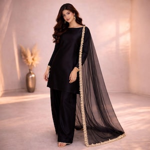 May include: A black two-piece outfit featuring a long-sleeved tunic and wide-leg pants. A sheer black scarf with gold trim drapes over the shoulders. The outfit is worn by a person with long, wavy brown hair.