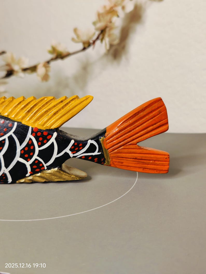 May include: A hand-painted wooden fish sculpture with a black body, white scale pattern, and red polka dots. The fins are yellow and orange. The fish is a decorative item.