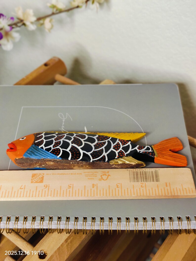 May include: A hand-carved wooden fish figurine with orange, black, and yellow details. The fish has a detailed scale pattern and a vibrant orange tail. The fish is approximately 10 inches long.