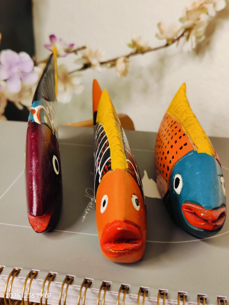 May include: Three hand-painted wooden fish sculptures. The fish have vibrant colors, including orange, blue, and red. Each fish has a unique design, with details like scales and fins. The sculptures are decorative and add a touch of whimsy.