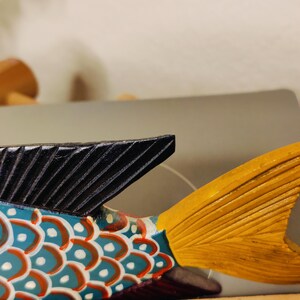 May include: A colorful wooden fish sculpture with a black dorsal fin and a yellow tail fin. The body is painted with blue, red, and white patterns. The sculpture is a decorative item.