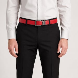 Op de afbeelding: Een felrode riem met een rechthoekige metalen gesp, gedragen bij een lichtgrijs overhemd en een zwarte broek. De riem heeft een gladde afwerking en een standaard gespsluiting, wat zorgt voor een opvallend contrast met de donkere broek.
