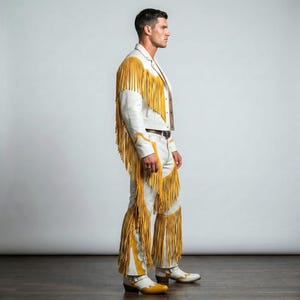 Puede incluir: Un conjunto de chaqueta y pantal&oacute;n de cuero blanco con largos flecos de color amarillo vibrante a lo largo de las mangas, los hombros y las piernas. El atuendo incluye una chaqueta con cuello y cremallera y un pantal&oacute;n con cintur&oacute;n marr&oacute;n.