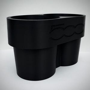 May include: Black car cup holder with two cup slots and a small tray. The cup holder has the number "500" embossed on the side. The cup holder is made of a matte black material.