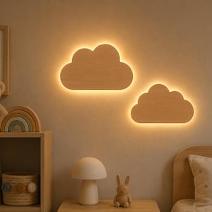 Könnte beinhalten: Zwei wolkenförmige Wandleuchten aus hellem Holz. Jede Lampe hat eine glatte, abgerundete Silhouette und strahlt ein sanftes, warmes Licht von ihren Rändern aus, wodurch ein Halo-Effekt auf der Wandoberfläche entsteht, an der sie montiert sind.