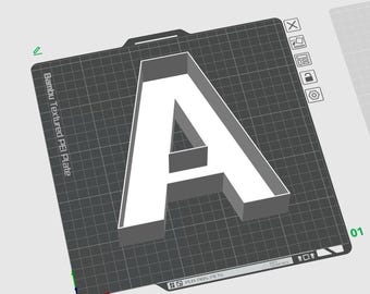 May include: A 3D-rendered white letter "A" on a dark gray textured surface. The letter is elevated, with a box-like structure. The surface has a grid pattern and text that reads "Bambu Textured PEI Plate".