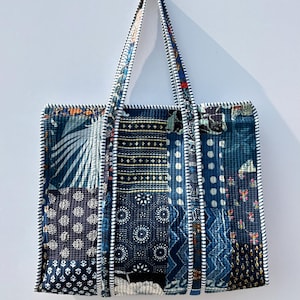 Może przedstawiać: Torba typu tote patchwork z różnymi wzorami niebieskiej tkaniny. Torba ma prostokątny kształt z dwoma uchwytami i biało-czarnym paskiem. Żółta uśmiechnięta buzia znajduje się na ścianie za torbą.