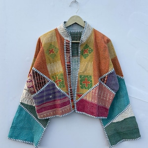 May include: A cropped jacket constructed from multicolored patchwork fabric featuring various geometric and floral patterns in shades of yellow, orange, pink, teal, and green. The garment has long sleeves, a collarless neckline, and visible stitching.