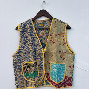 May include: A sleeveless vest featuring a patchwork design of various floral and geometric patterns in shades of blue, tan, green, and red. The garment has two front pockets with contrasting yellow and white striped trim along the edges.