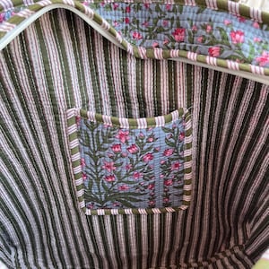 May include: A quilted tote bag with a striped interior in olive green and pink. The interior features a floral print pocket and trim. The bag has a zipper closure and matching handles.