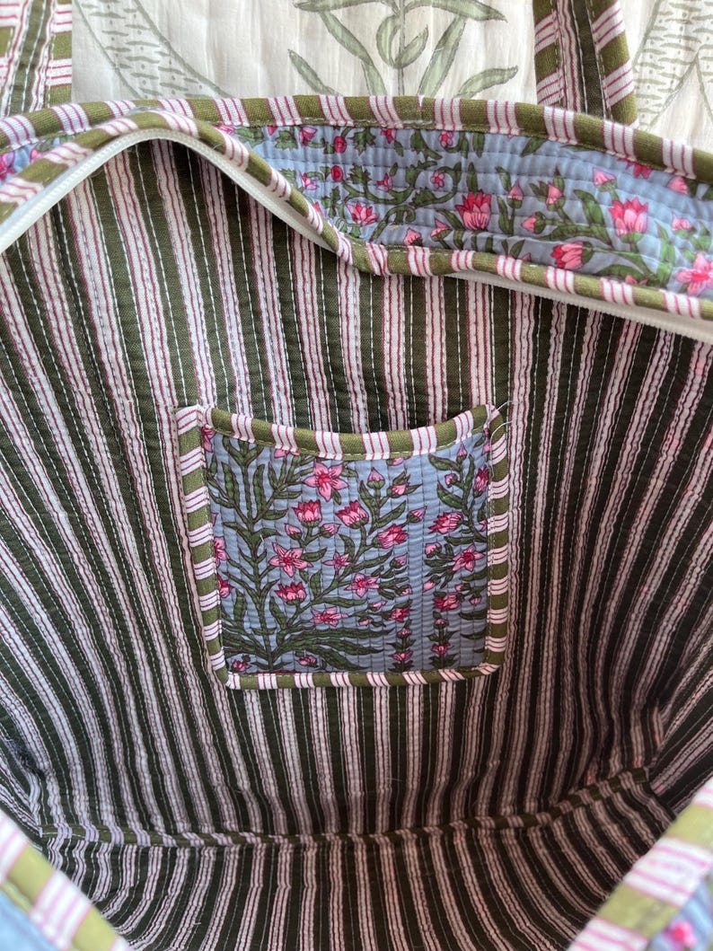 May include: A quilted tote bag with a striped interior in olive green and pink. The interior features a floral print pocket and trim. The bag has a zipper closure and matching handles.