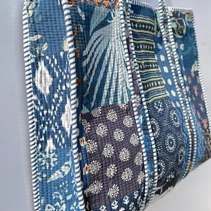 May include: A patchwork tote bag with a variety of blue fabric patterns. The bag features a quilted design with white and blue striped trim and handles. The bag is approximately 15 inches wide and 14 inches tall.