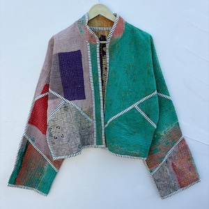 May include: A cropped jacket made from quilted patchwork fabric featuring a vibrant green panel on the right side and various multicolored patterned sections on the left, all finished with black and white striped trim along the edges.