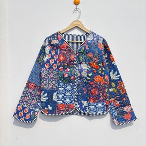 May include: A quilted jacket with a patchwork design featuring floral patterns in shades of blue, red, and pink. The jacket has a V-neck and is lined with a black and white striped fabric. The edges are finished with a scalloped trim.