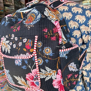 以下が含まれることがあります： 赤と白のストライプのトリムが付いた、黒いフローラルプリントのバックパック。バックパックは、さまざまなカラフルな花と葉のキルティングデザインが特徴です。バッグには2つのサイドポケットと調節可能なストラップが付いています。