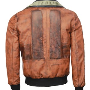 May include: A brown leather jacket with a distressed finish. The jacket features a ribbed collar, two vertical panels on the back, and black ribbed cuffs and hem. The leather has a worn appearance with darker patches.