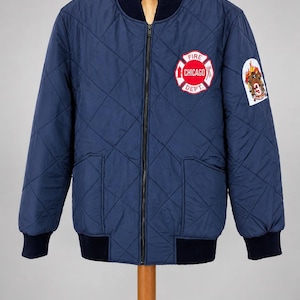 Peut inclure: Un blouson aviateur matelassé bleu marine avec un col, des poignets et un ourlet côtelés bleu foncé. L'avant présente un écusson circulaire avec le texte FIRE CHICAGO DEPT et un graphique d'échelle et de hache. Un écusson sur la manche montre un chien.