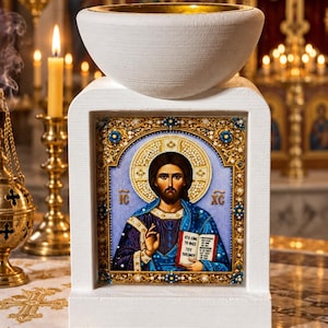 Könnte beinhalten: Ein weißer rechteckiger Ständer mit einer zentralen religiösen Ikone von Jesus Christus in blau-goldenen Gewändern, der ein Buch mit griechischem Text hält. Der Ständer ist mit einem weißen, schalenförmigen Becken mit goldener Innenseite versehen.