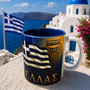 Pode incluir: Uma caneca de cerâmica com um gráfico da bandeira grega em azul e branco, uma ilustração de uma coluna jónica dourada e o texto grego "ΕΛΛΑΣ" em letras douradas. A caneca tem exterior branco, interior azul escuro e uma pega branca.