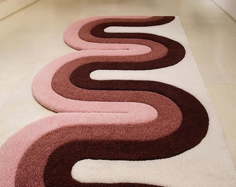 以下が含まれることがあります： ピンク、ブラウン、白の波模様が特徴的なレトロスタイルのラグ。 流れのある川や様式化された小道を連想させるデザインで、ヴィンテージ感をプラス。 柔らかく、ふわふわした素材で作られており、リビングルームや寝室に最適です。