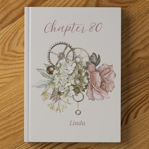 Puede incluir: Un libro de tapa dura con un diseño floral y de engranajes. La portada presenta el texto "Chapter 80" en una fuente cursiva, junto con el nombre "Linda". El arreglo floral incluye una rosa rosa y flores blancas.