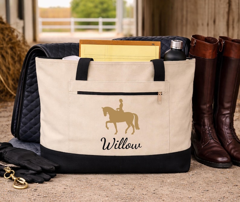 A beige tote bag with a black bottom and handles. A gold silhouette of a horse and rider is on the front, with the name "Willow" below. A pair of brown riding boots stands next to the bag.